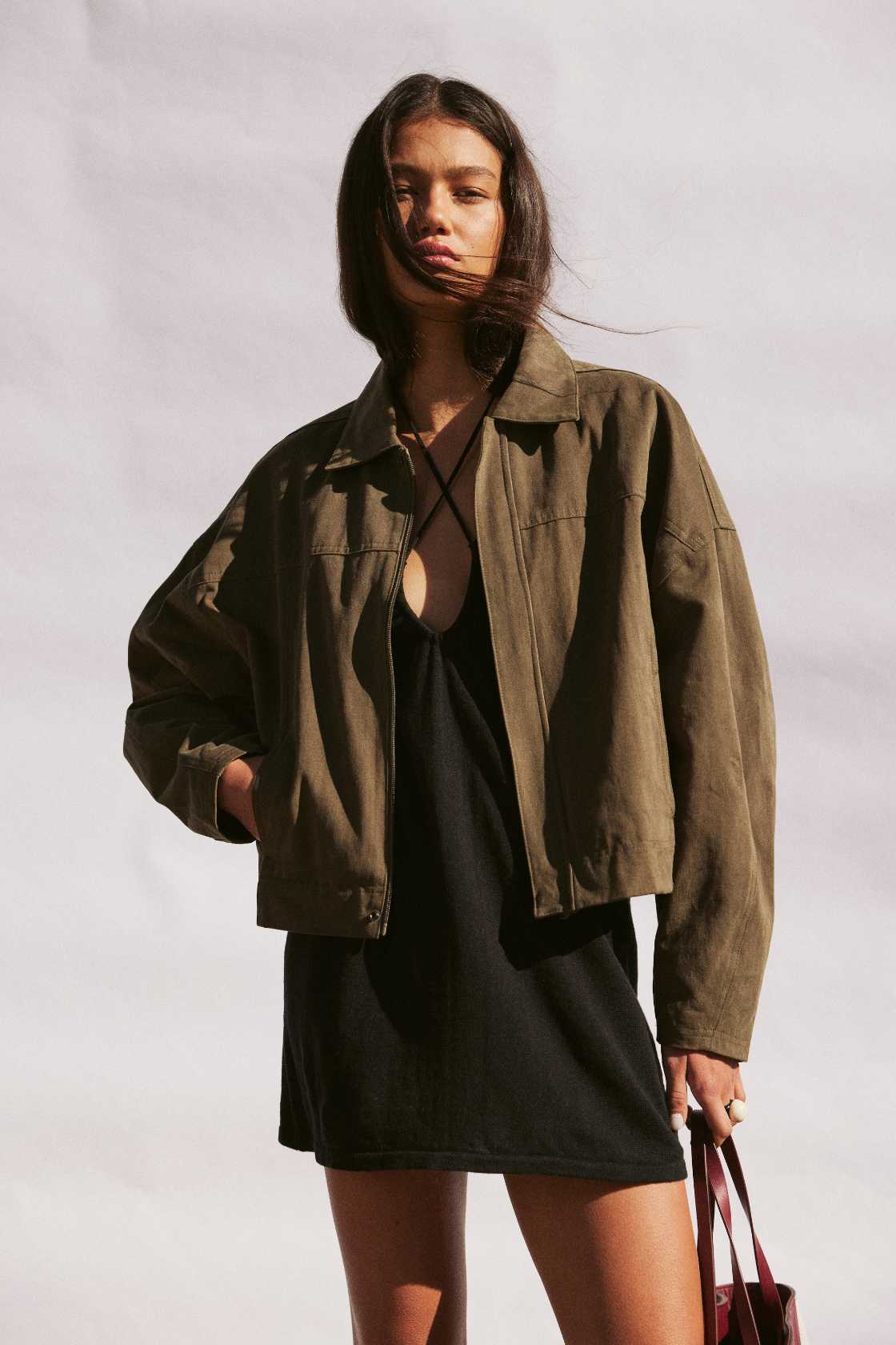 Model wearing khaki cotton jacket with velvet finish, cropped boxy fit and wide sleeves, styled over a black slip dress outdoors