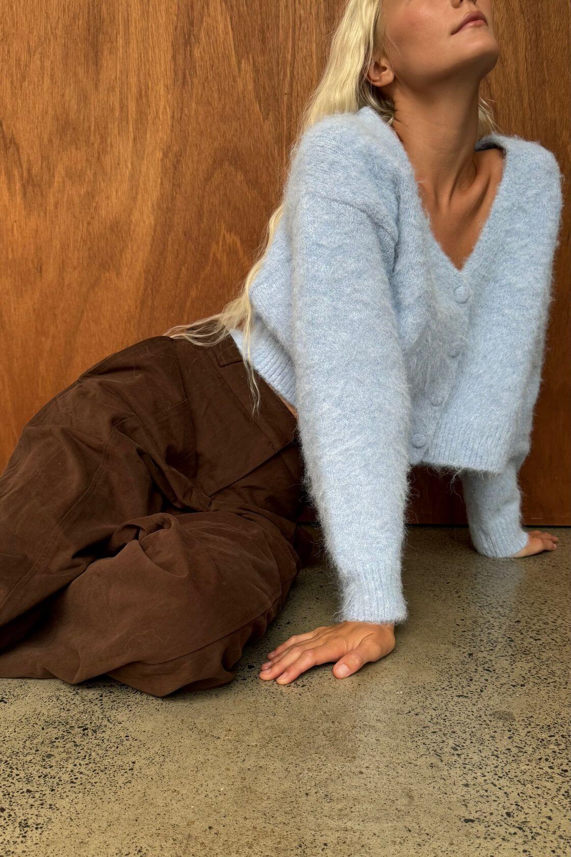 Model wearing a soft sky blue fluffy knit cardigan with a deep V neckline and button-front closure, styled with relaxed espresso wide-leg pants.
