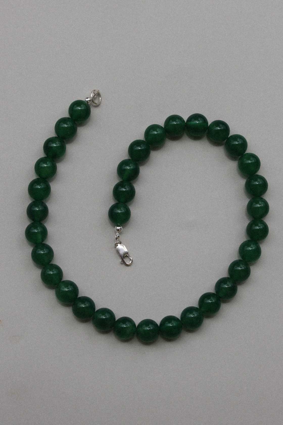 Green chalcedony gemstone necklace shown in a gentle curve, highlighting the round beads and silver clasp on a neutral surface.