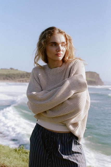 Lifestyle image of cream knit sweater worn outdoors by the ocean