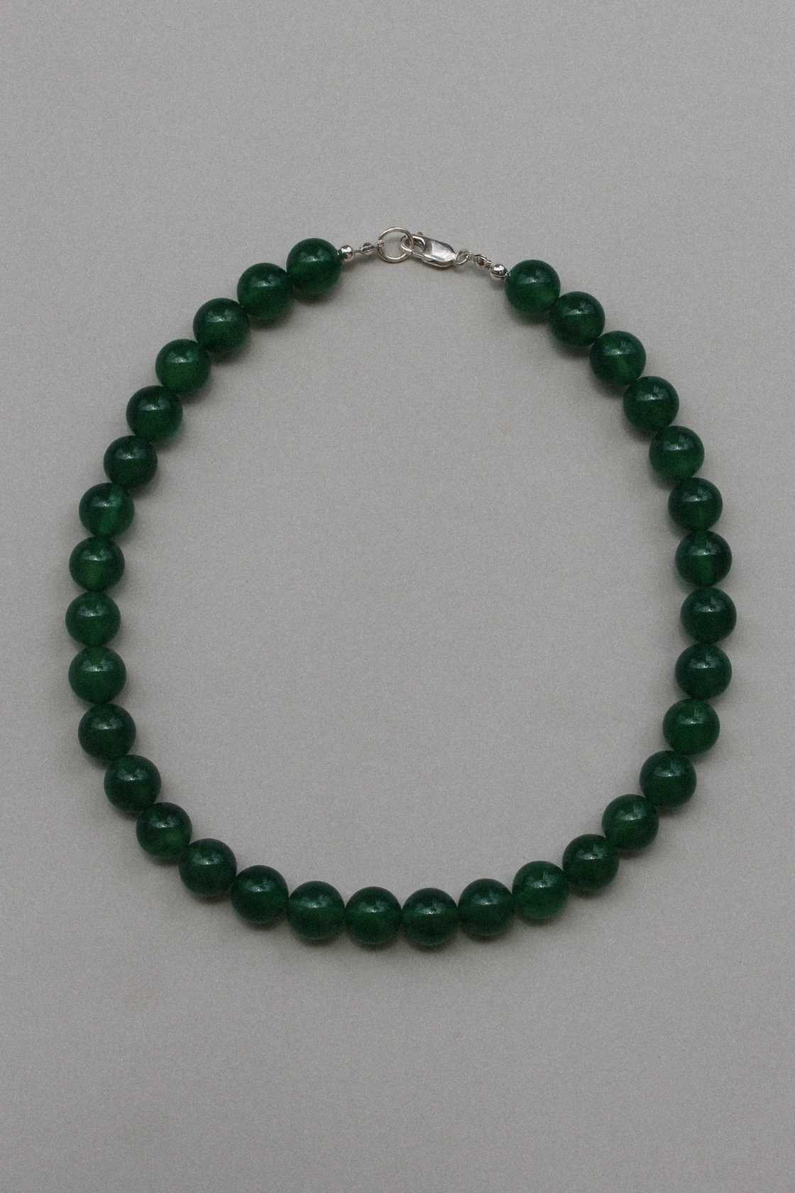 Green chalcedony beaded necklace with sterling silver clasp, laid in a circle on a soft grey background.