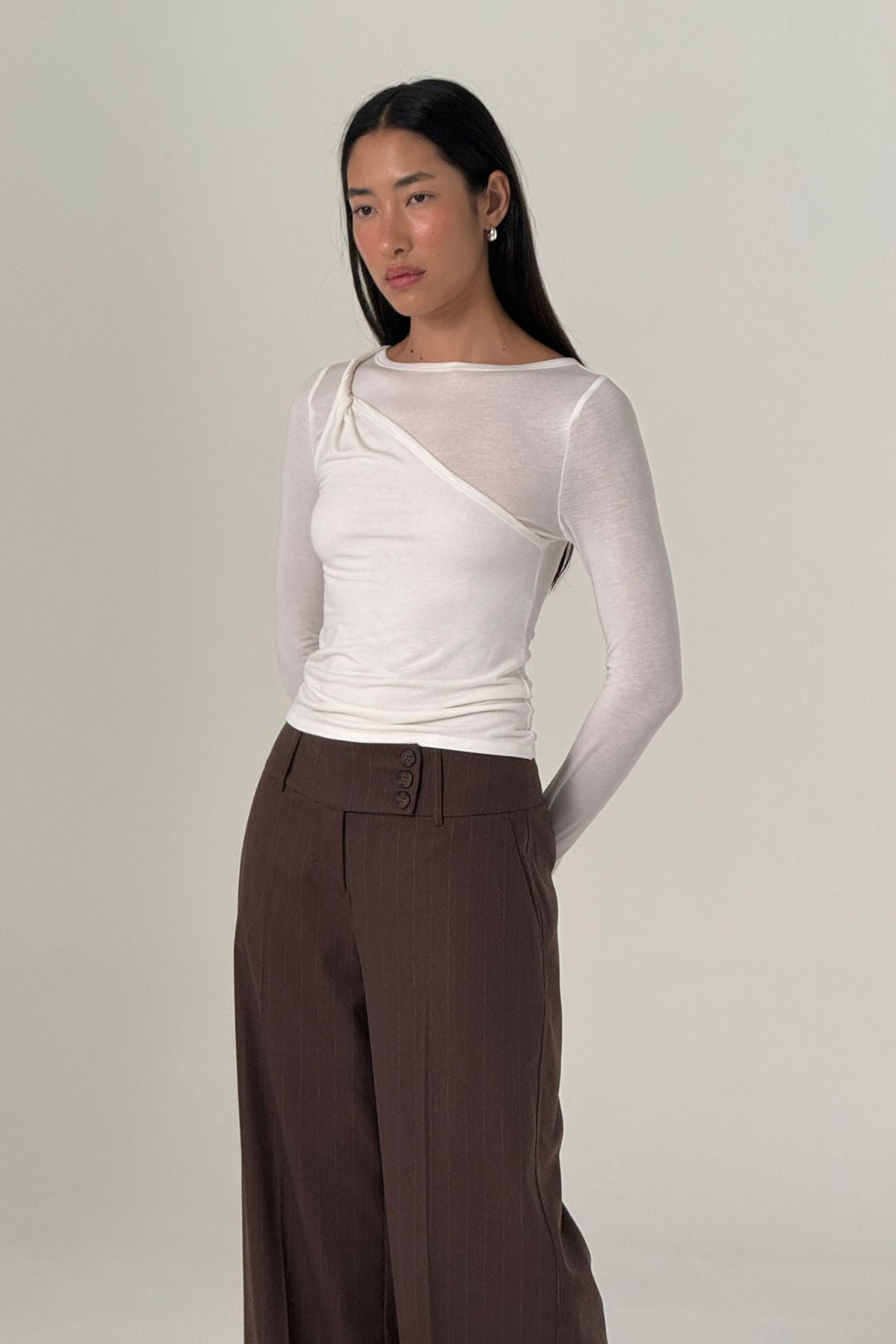 Model wearing Mabel LS in cream against white wall with Manon trousers in espresso pinstripe. 