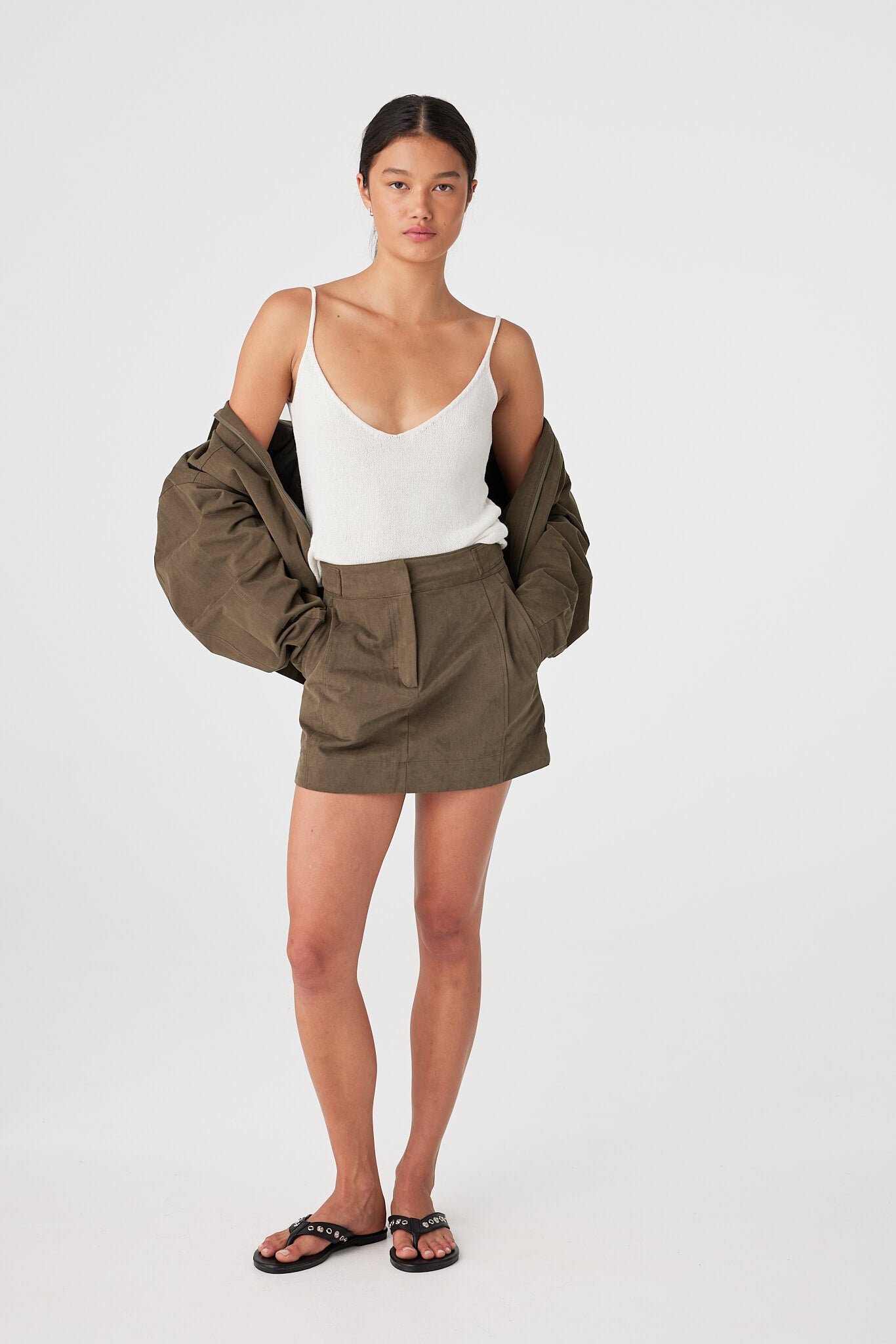 Model wearing khaki cotton mini skirt with velvet finish, structured shape with side seam pockets, styled with a white tank