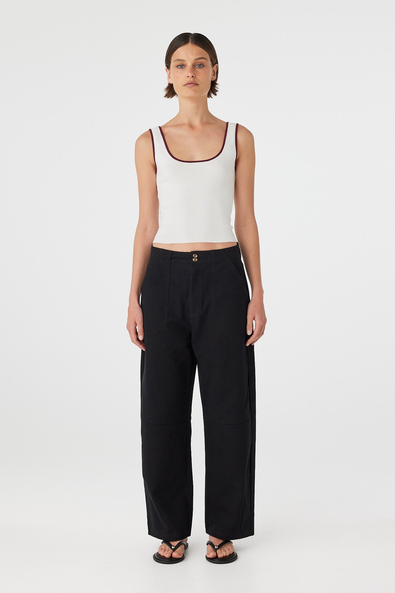 Model wearing Akira Pant in black, relaxed barrel-leg cotton pants with zip fly and patch pockets, full length front view.