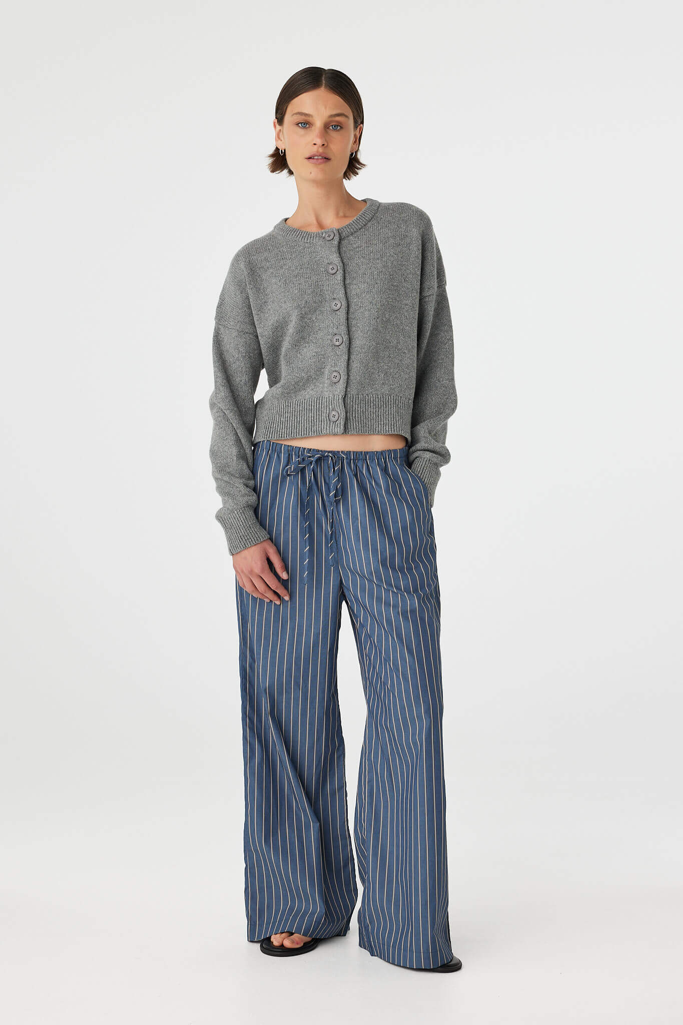 Full body front view of Bobby Cardigan grey marle, relaxed fit with dropped shoulder, styled with blue stripe pants.