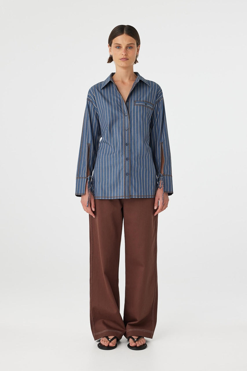 Full body front view of Blair Shirt muted blue stripe, relaxed cotton shirt styled with brown pants.