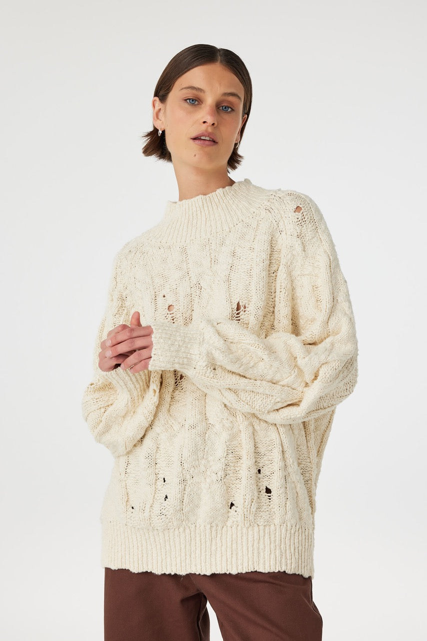 Front view of cream chunky cable knit sweater with funnel neck and small hole detail