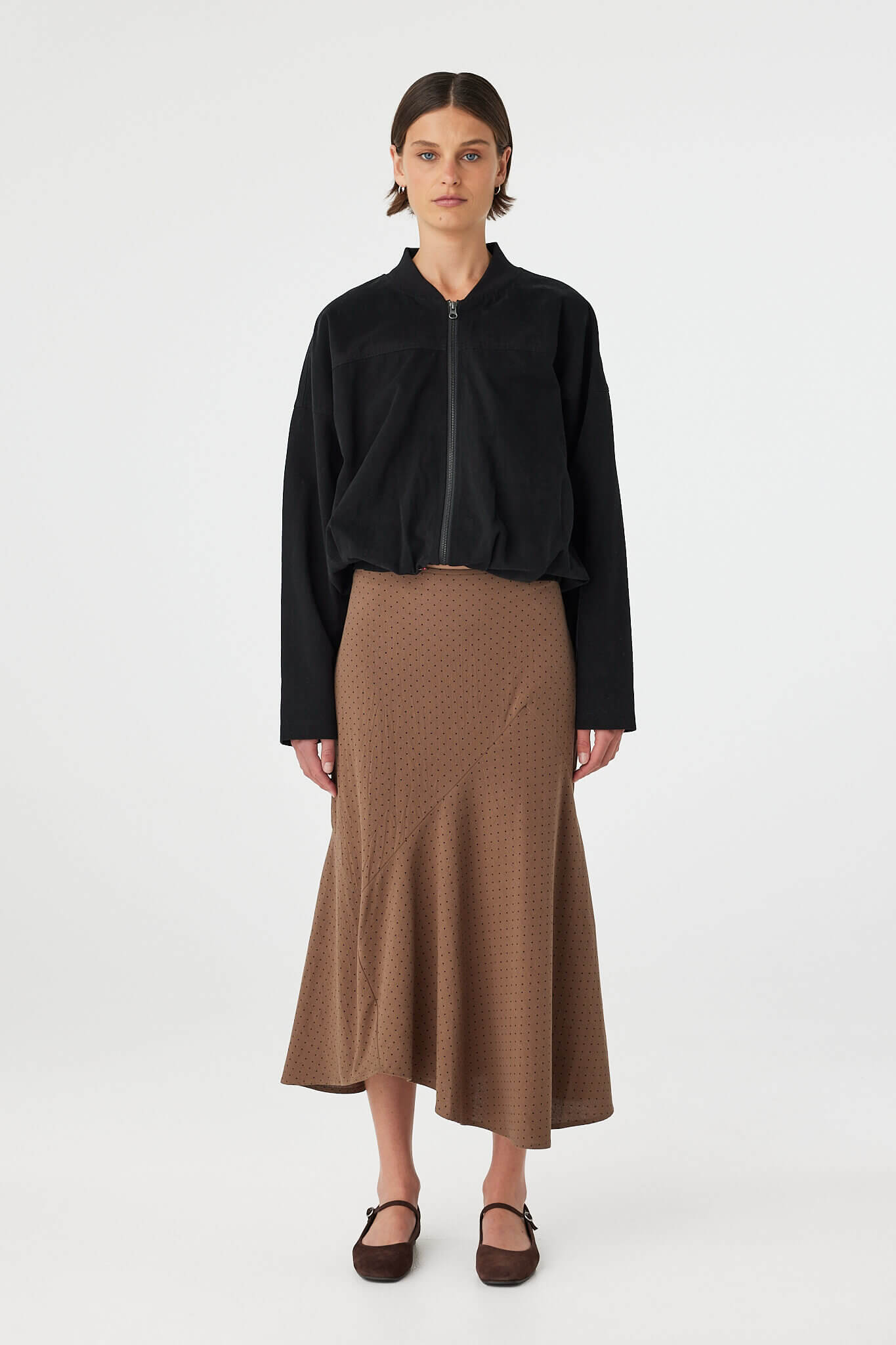 Model wearing Alessia Skirt in choc polka dot, fitted waist cotton A-line skirt with asymmetrical hem, front view.