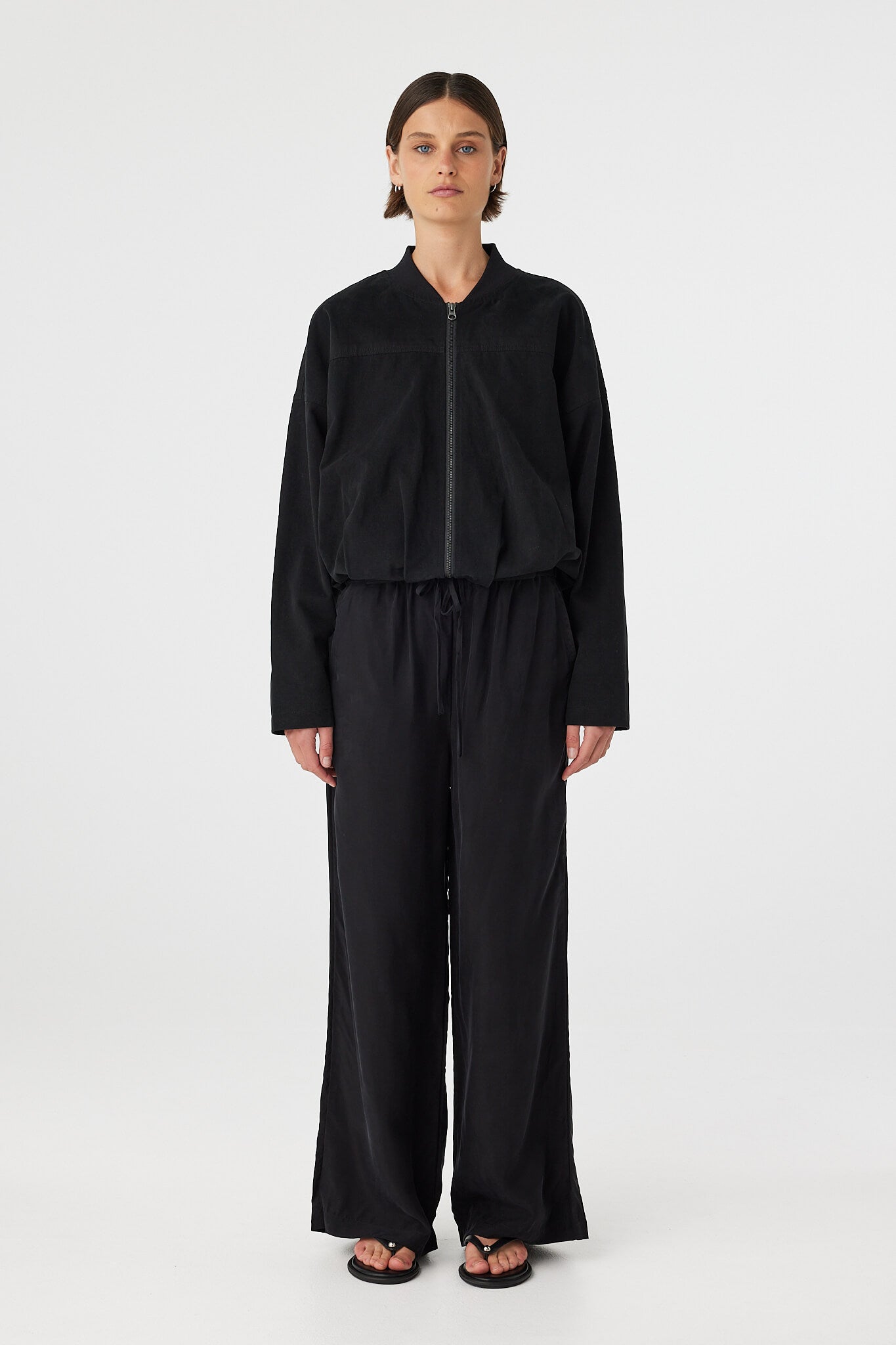 Model wearing Rae Pant in black, straight-leg cupro–rayon pants with elastic drawcord waistband, full front view.