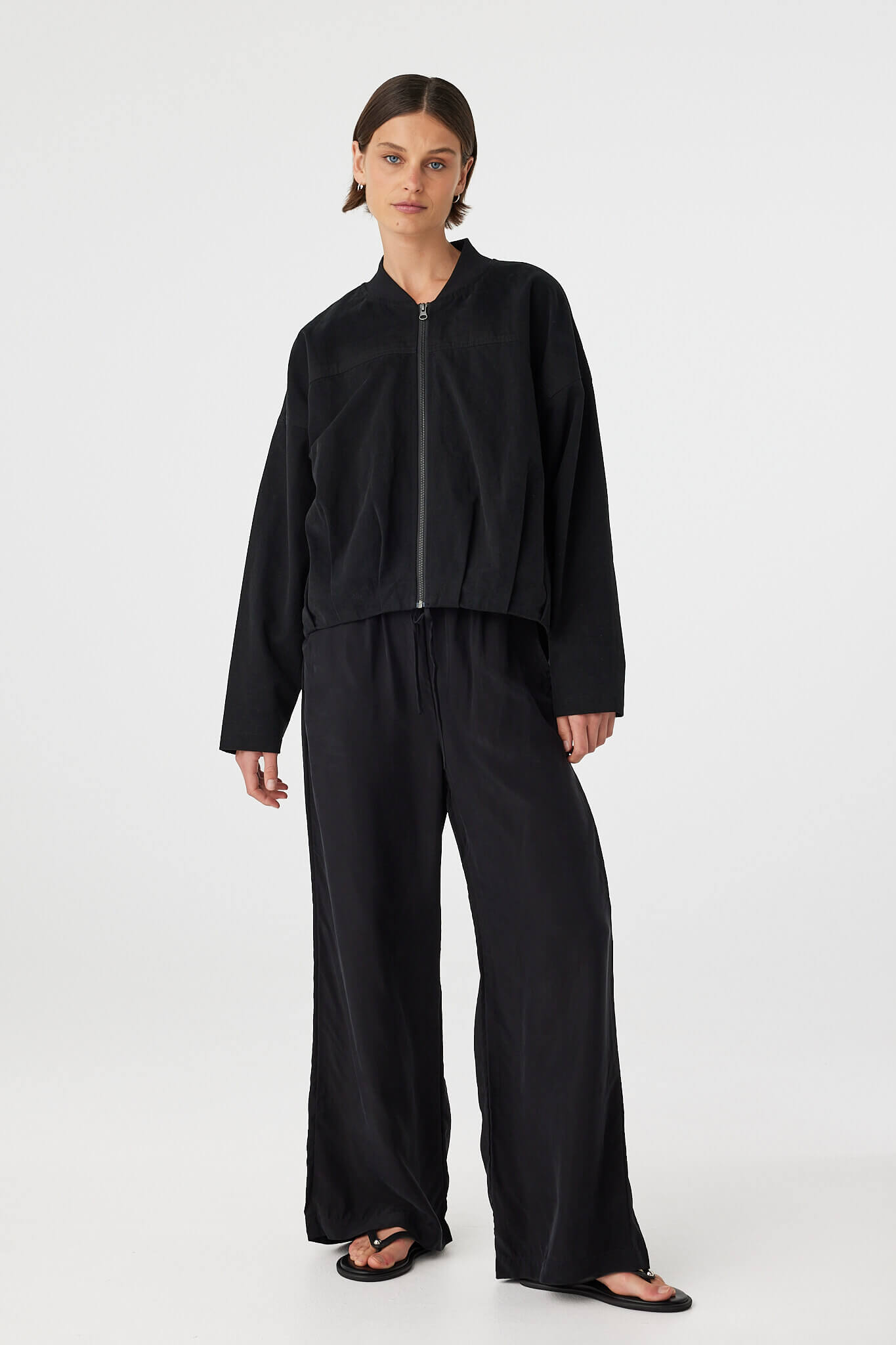 Full body front view of black bomber jacket styled with wide-leg pants