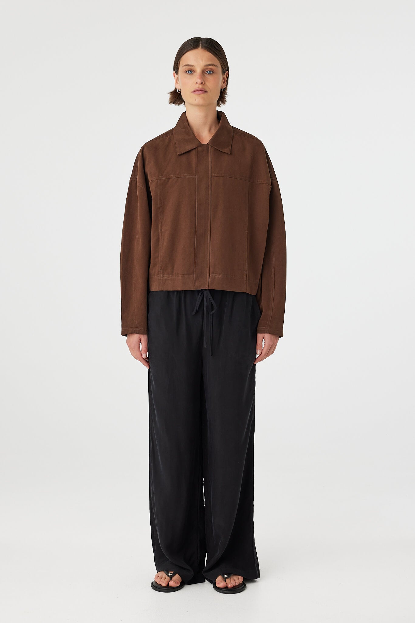 Eames jacket in espresso worn front on, showcasing the cropped boxy fit, clean front panel and concealed zipper, styled with black wide-leg pants and sandals