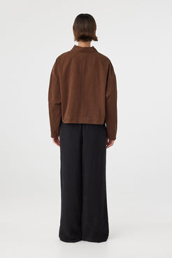 Eames jacket in espresso viewed from back, featuring a clean silhouette with subtle seam detailing and waistband tabs, styled with black pants and sandals