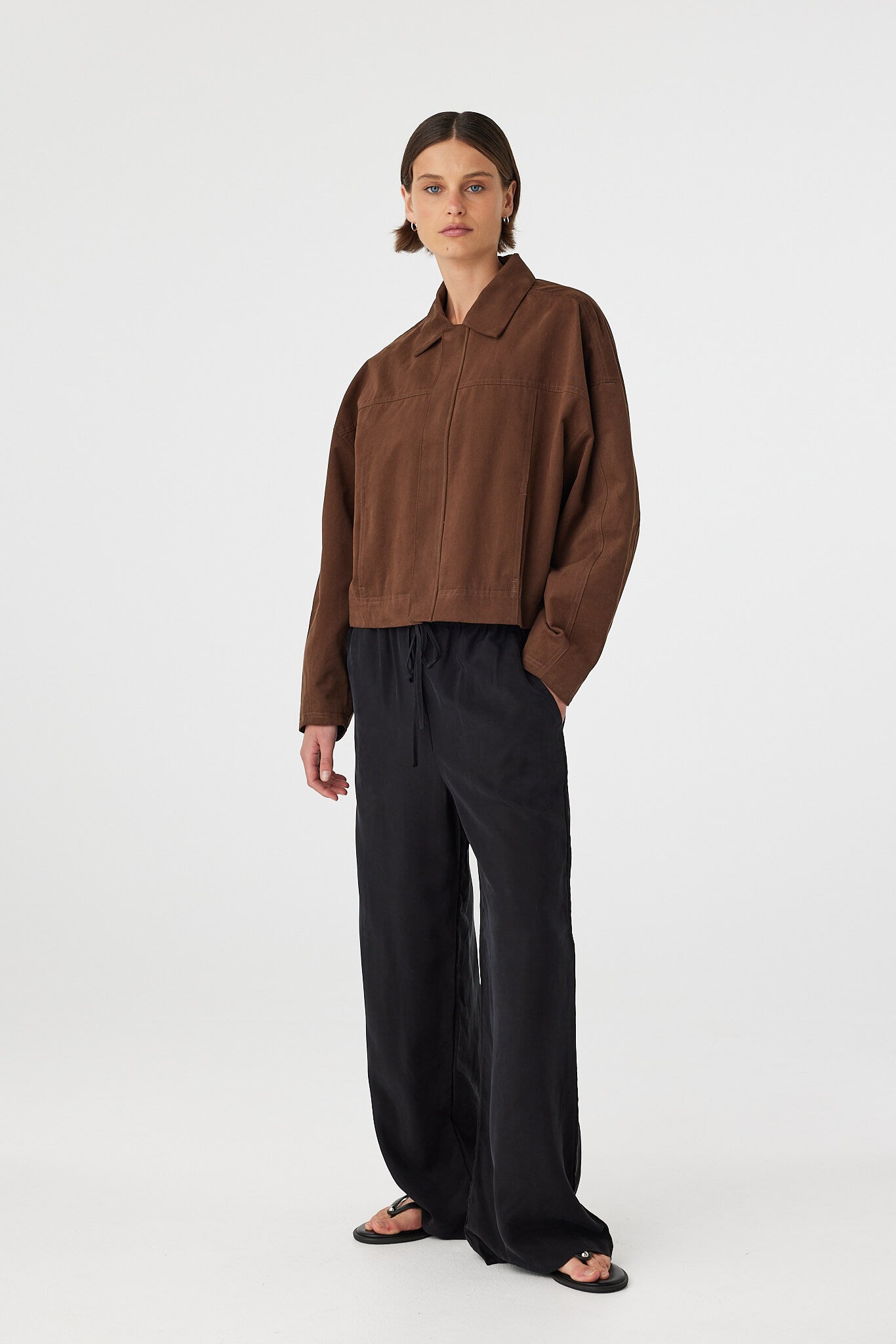 Eames jacket in espresso worn at an angle, showing the concealed front zipper, structured collar and relaxed fit, styled with black pants and sandals