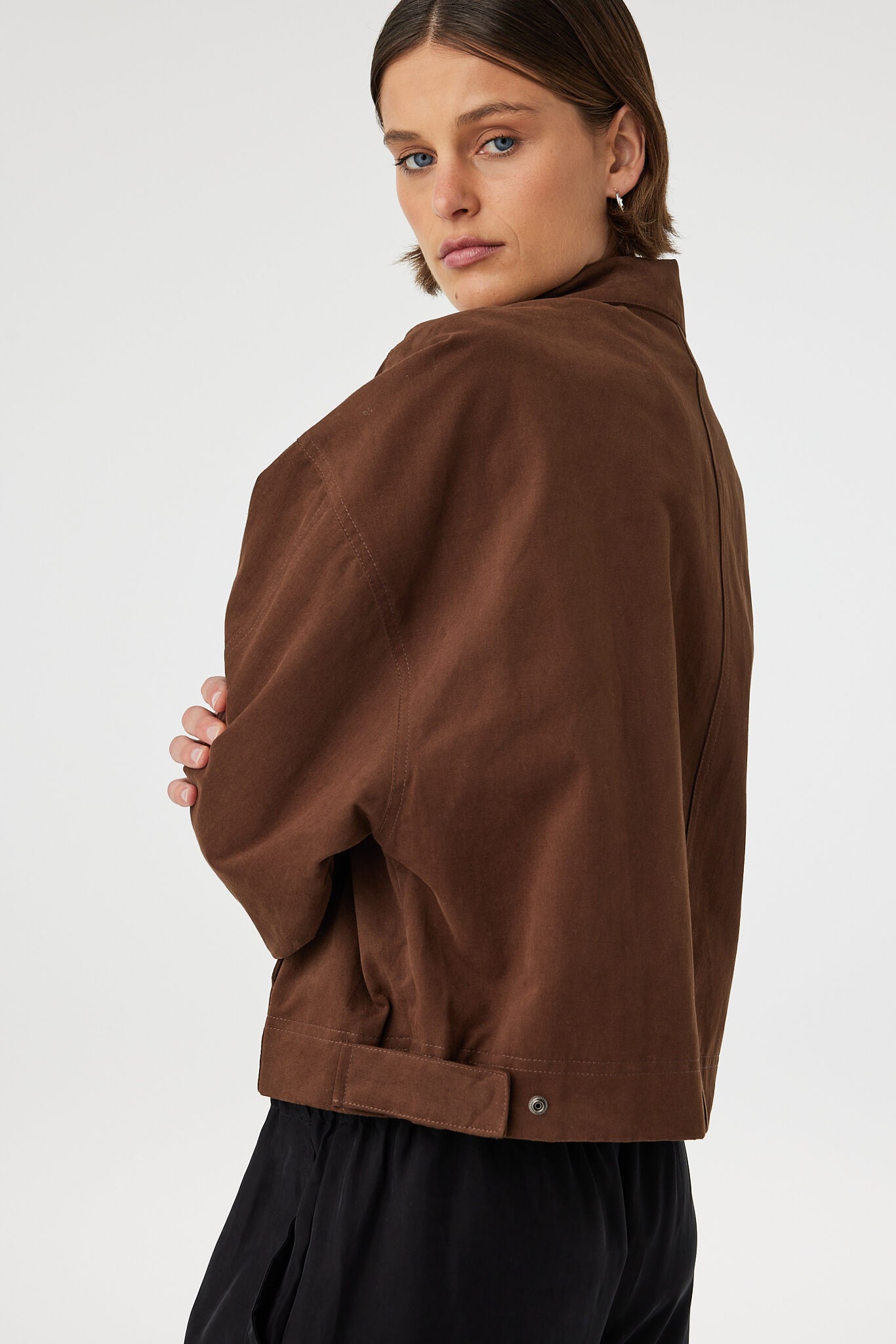 Eames jacket in espresso worn from a back angled view, showing the smooth finish, seam lines and side tab detail at the waistband