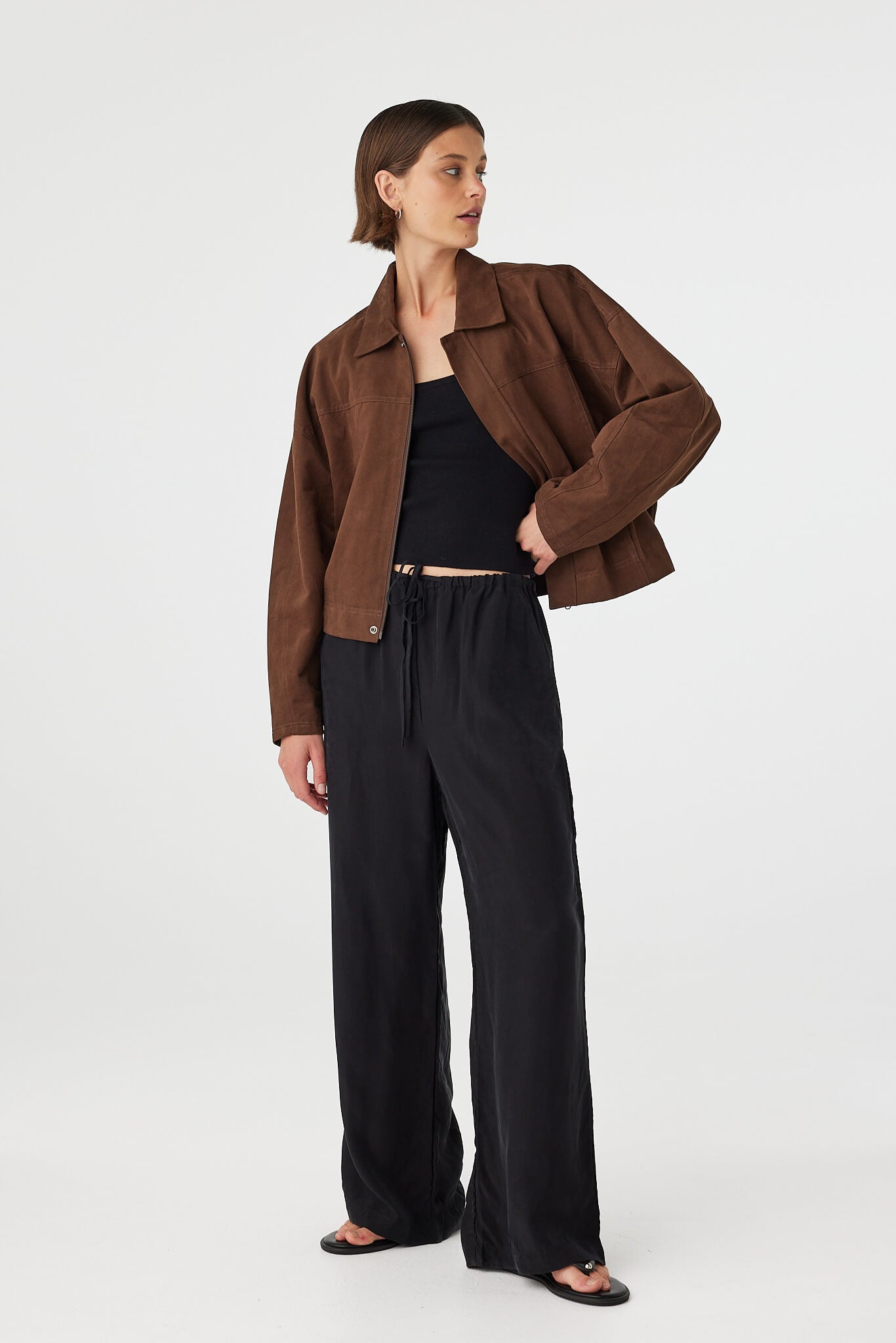 Eames jacket in espresso worn at an angle open, showcasing the soft cotton finish, structured collar and cropped silhouette, styled with black pants and sandals
