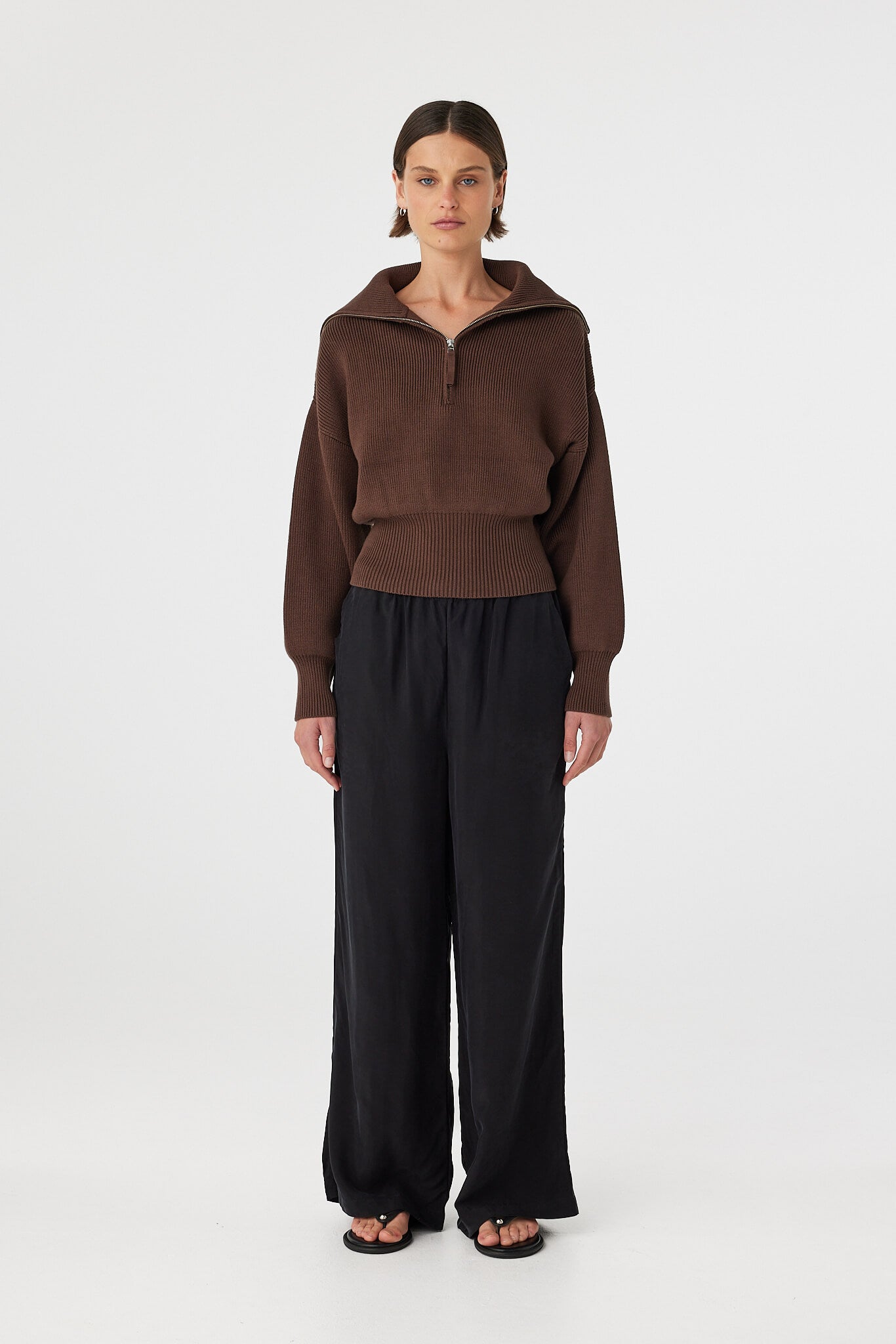 Marley zip sweater in espresso worn front on, showcasing the ribbed knit texture, exaggerated funnel neck collar and 1/4 zip detail, styled with black wide-leg pants and sandals