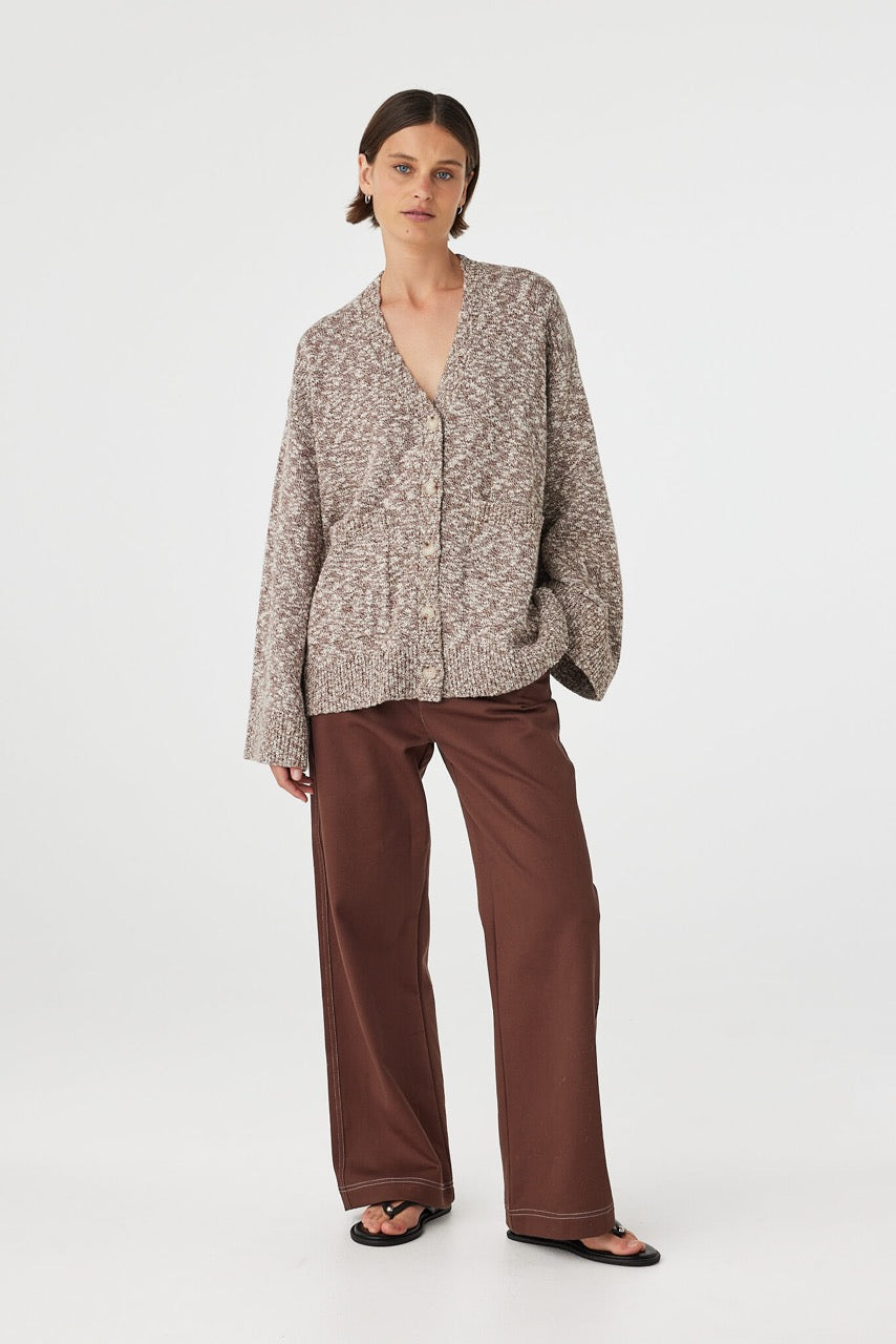 Emmet cardigan in chocolate and cream worn at an angle with hand in pocket, showcasing the relaxed fit, front patch pocket and textured finish, styled with brown pants and sandals