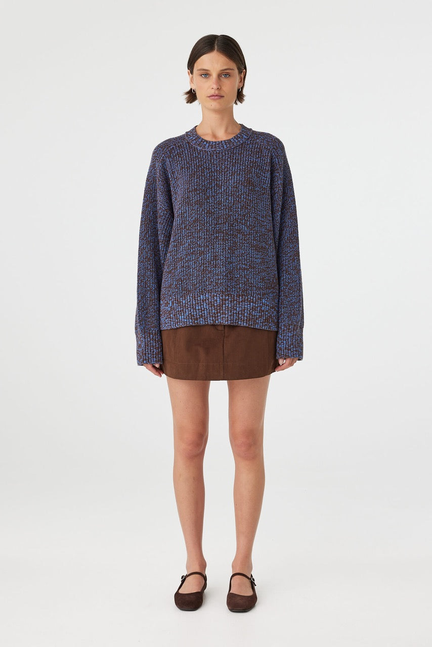Solene sweater in chocolate and royal blue mottled cotton knit worn front on, featuring an oversized fit, raglan sleeves and ribbed neckline, styled with a brown mini skirt and flats