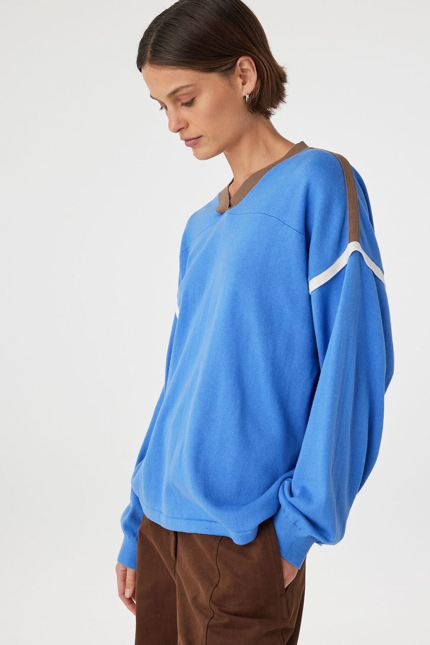 Relaxed fit long sleeve top in royal blue with espresso contrast trim, featuring dropped shoulders, oversized sleeves and soft drape, styled with brown trousers in a minimal studio setting