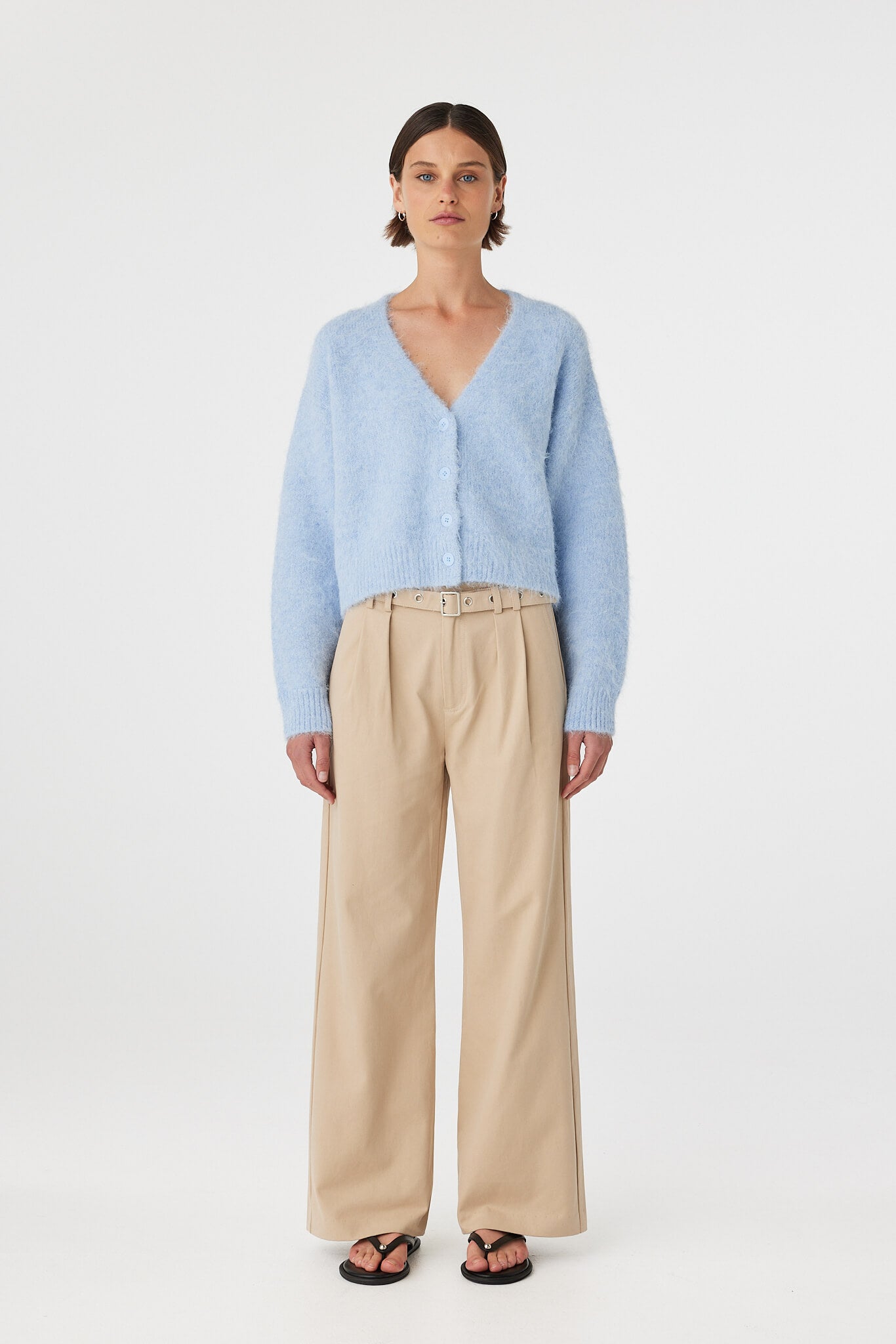 Liora fluffy cardigan in sky worn front on, featuring a button-up front, cropped length and relaxed silhouette, styled with beige trousers and black sandals

