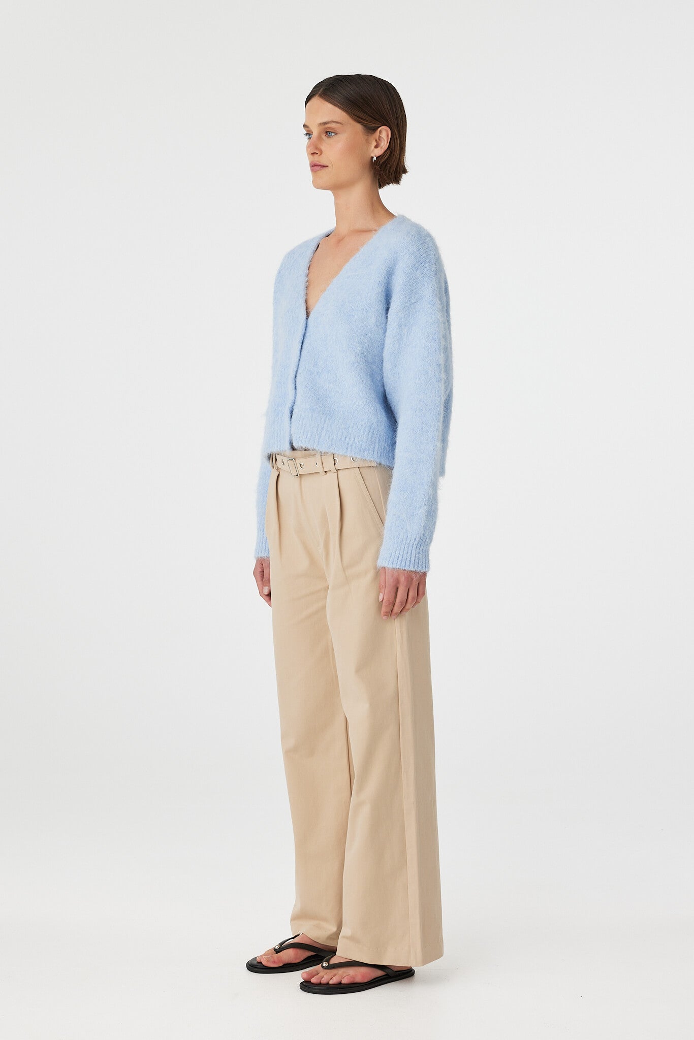 Liora fluffy cardigan in sky worn at an angle, showcasing the deep V neckline, button front and textured fluffy knit, styled with beige trousers and black sandals