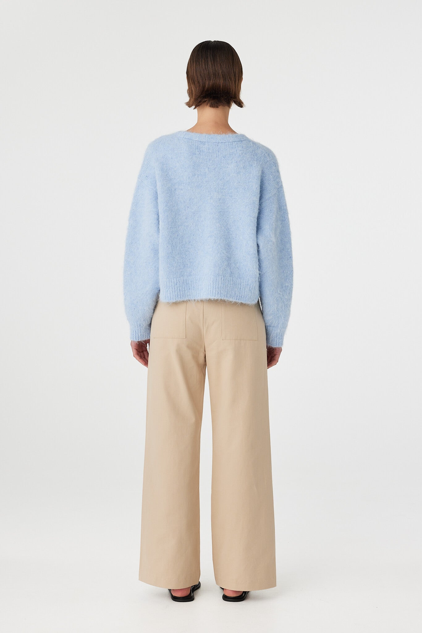 Liora fluffy cardigan in sky viewed from back, featuring a clean relaxed silhouette with ribbed hem and cuffs, styled with beige trousers and black sandals
