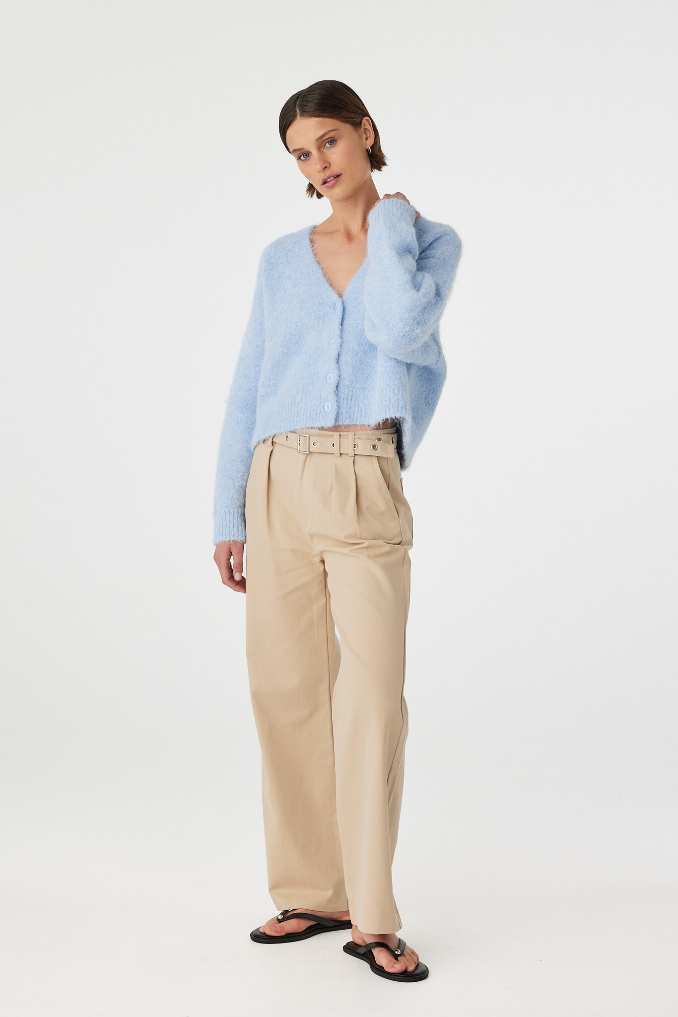 Liora fluffy cardigan in sky worn at an angle, showcasing the deep V neckline, button front and textured fluffy knit, styled with beige trousers and black sandals