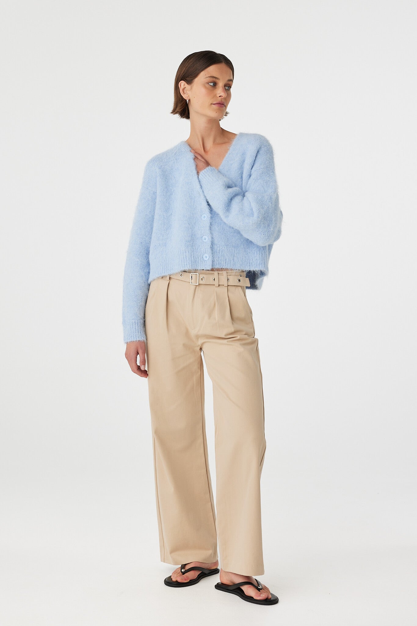 Liora fluffy cardigan in sky worn at an angle, showcasing the deep V neckline, button front and textured fluffy knit, styled with beige trousers and black sandals