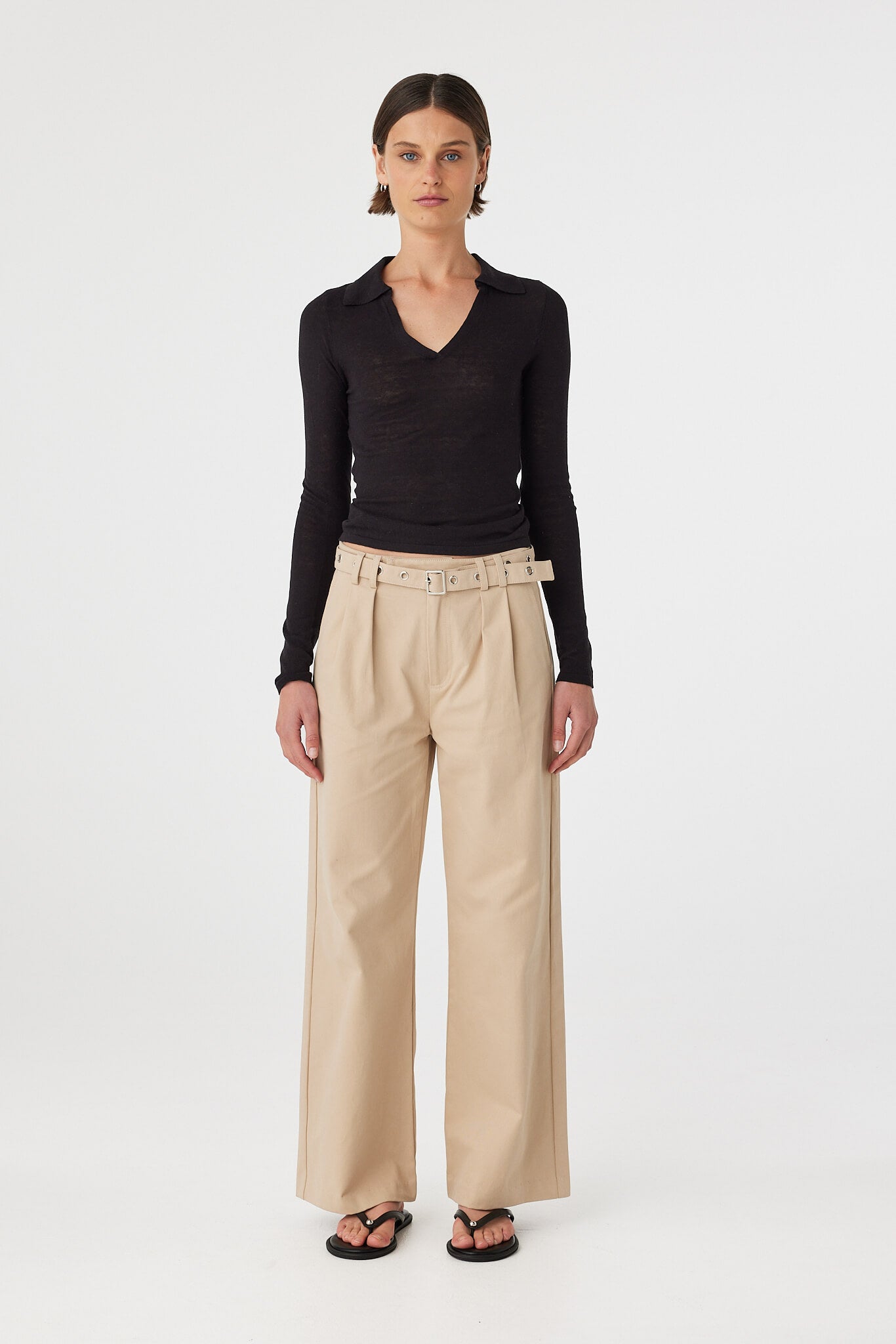 Mae longsleeve top in black worn front on, showcasing the slim fit silhouette, semi sheer knit texture and V neckline with polo collar, styled with beige wide-leg pants and sandals
