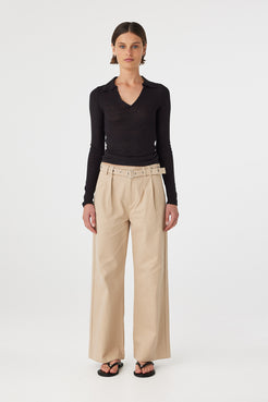 Mae longsleeve top in black worn front on, showcasing the slim fit silhouette, semi sheer knit texture and V neckline with polo collar, styled with beige wide-leg pants and sandals