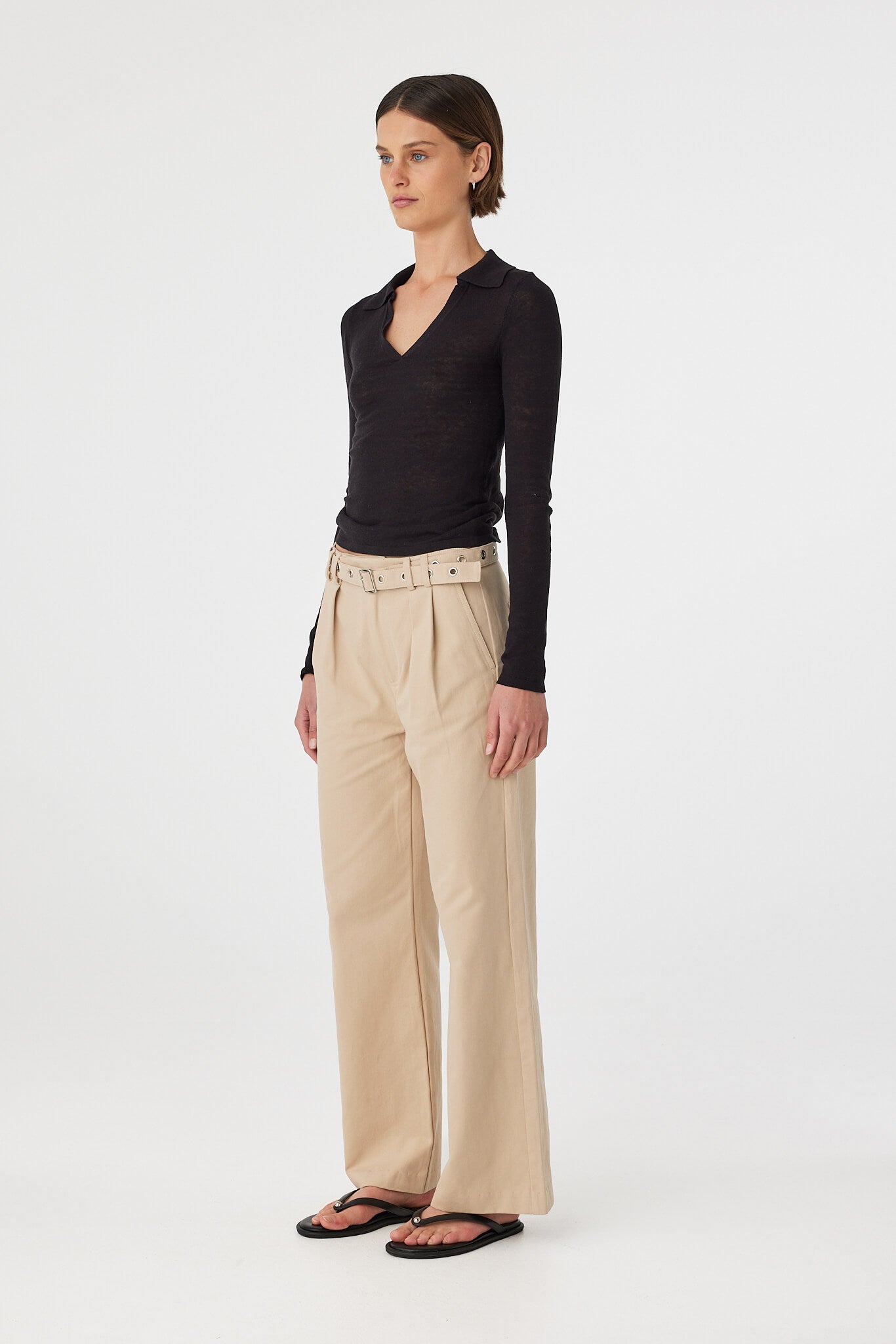 Mae long sleeve top in black shown in side profile, highlighting the fitted shape, long sleeves and lightweight knit finish, styled with taupe pants and sandals