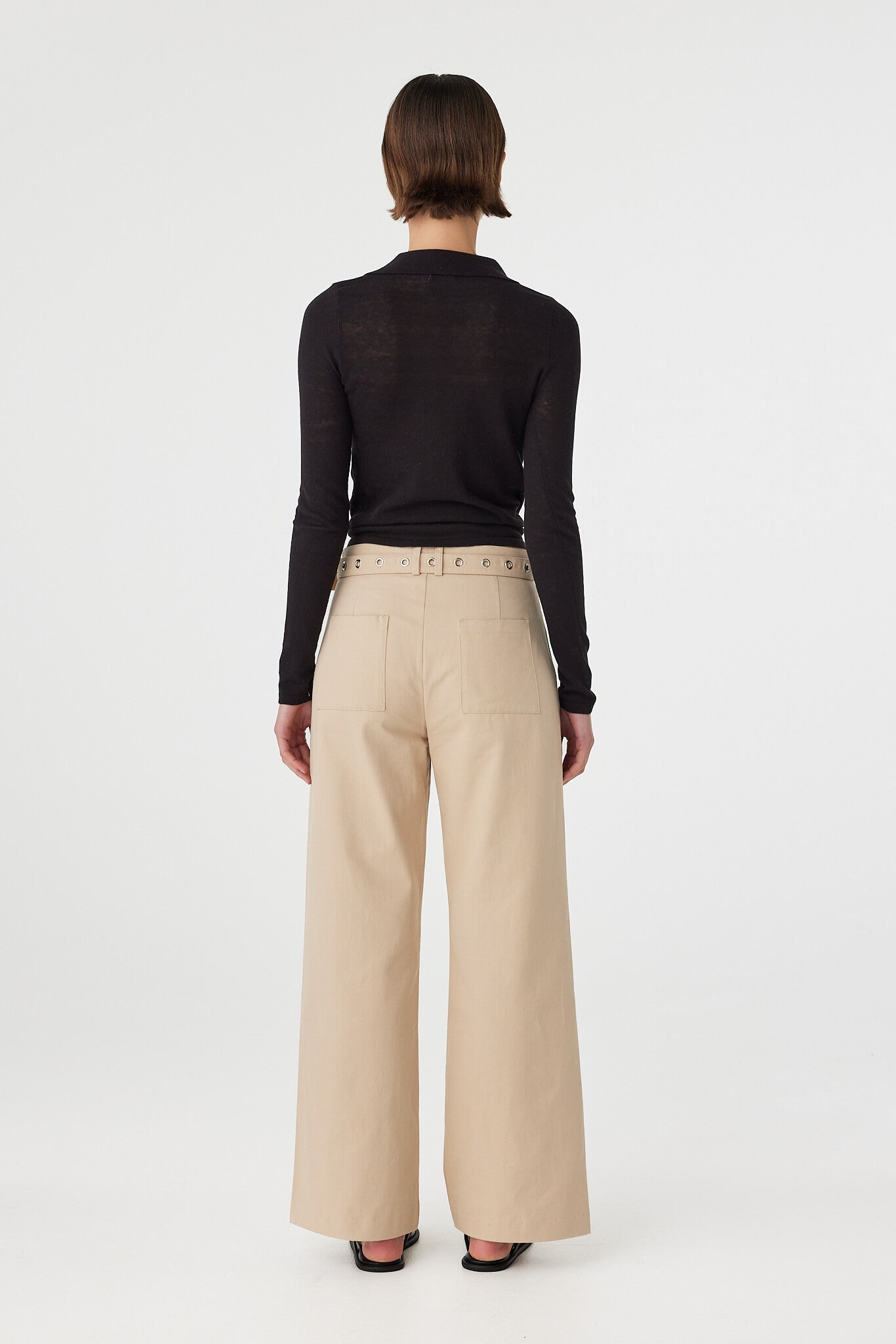 Mae long sleeve top in black viewed from back, featuring the clean slim fit and subtle semi sheer texture, styled with taupe pants and sandals