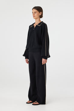 Nella zip sweater in black and taupe shown in side profile, highlighting the raglan sleeves, soft drape and contrast stripe detail along the arms, styled with black pants and sandals