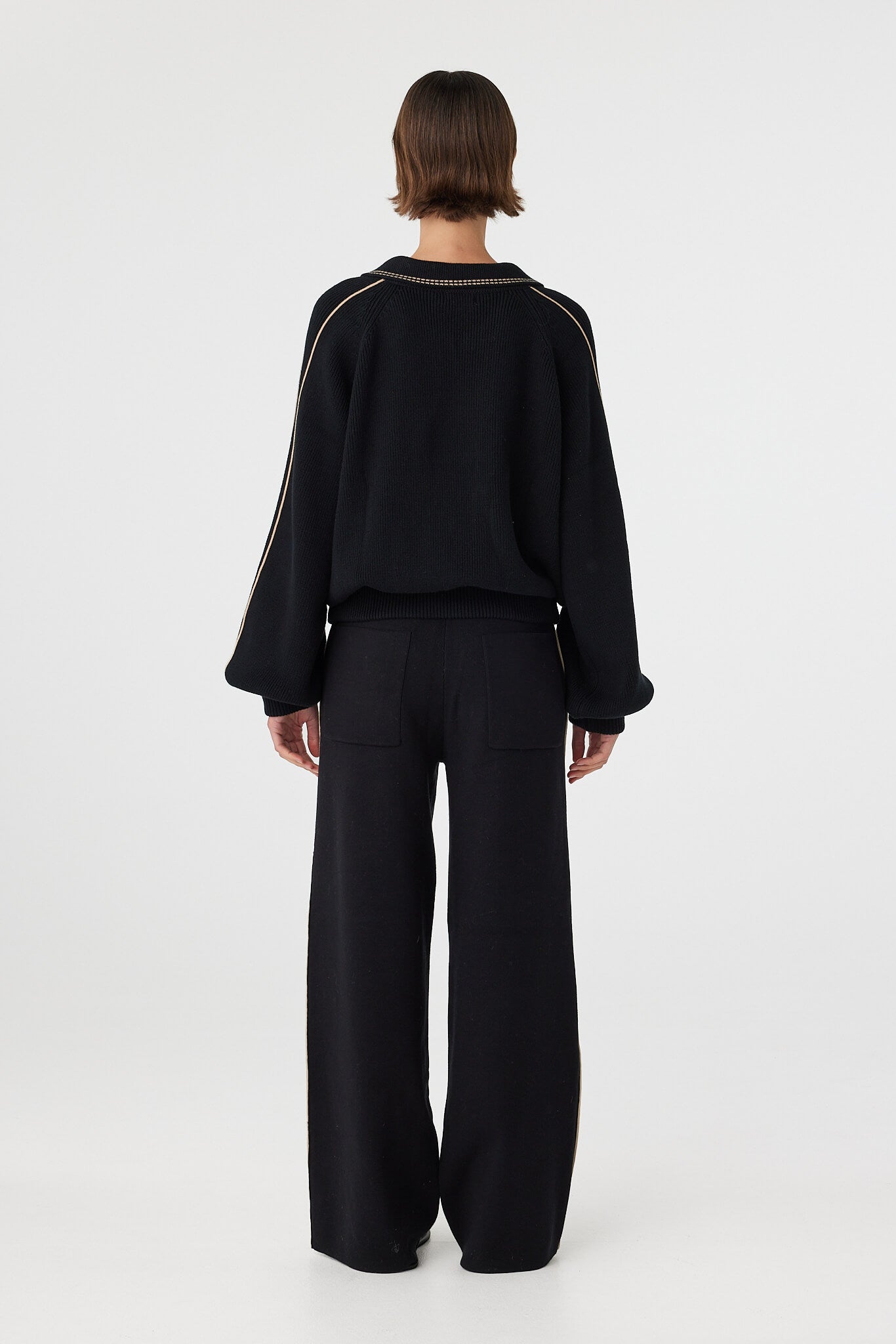 Nella zip sweater in black and taupe viewed from back, featuring the relaxed silhouette, ribbed waistband and subtle piping detail along the shoulders and sleeves