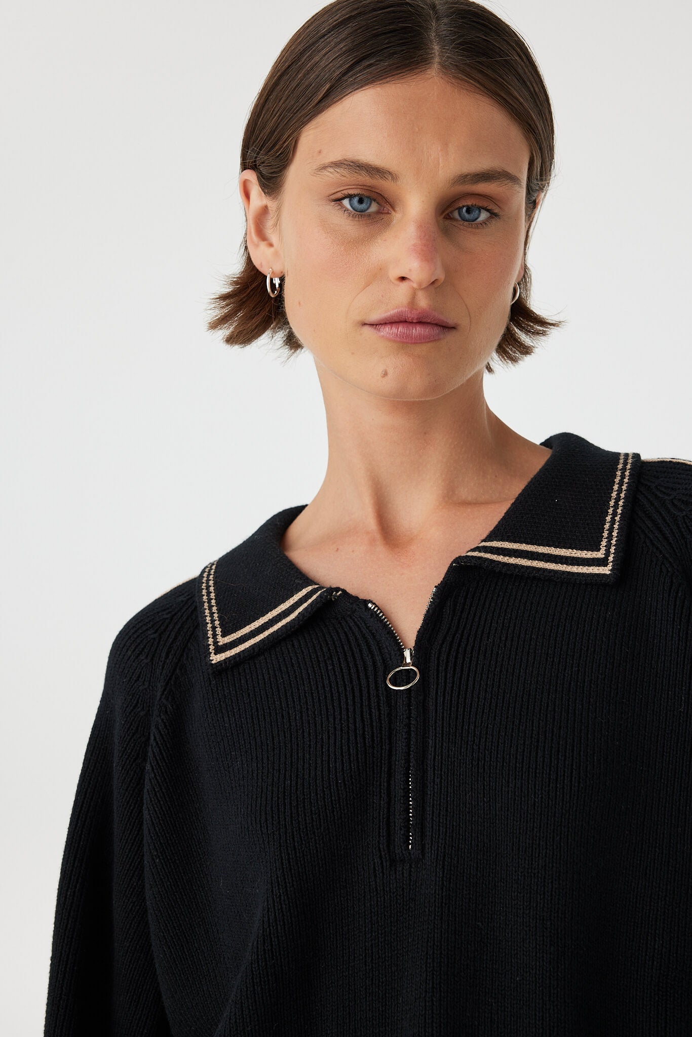Nella zip sweater in black and taupe close-up detail, showcasing the ribbed knit texture, contrast piping and metal zip at the neckline