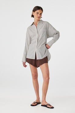 Three-quarter front view of black and white striped oversized shirt styled with brown shorts