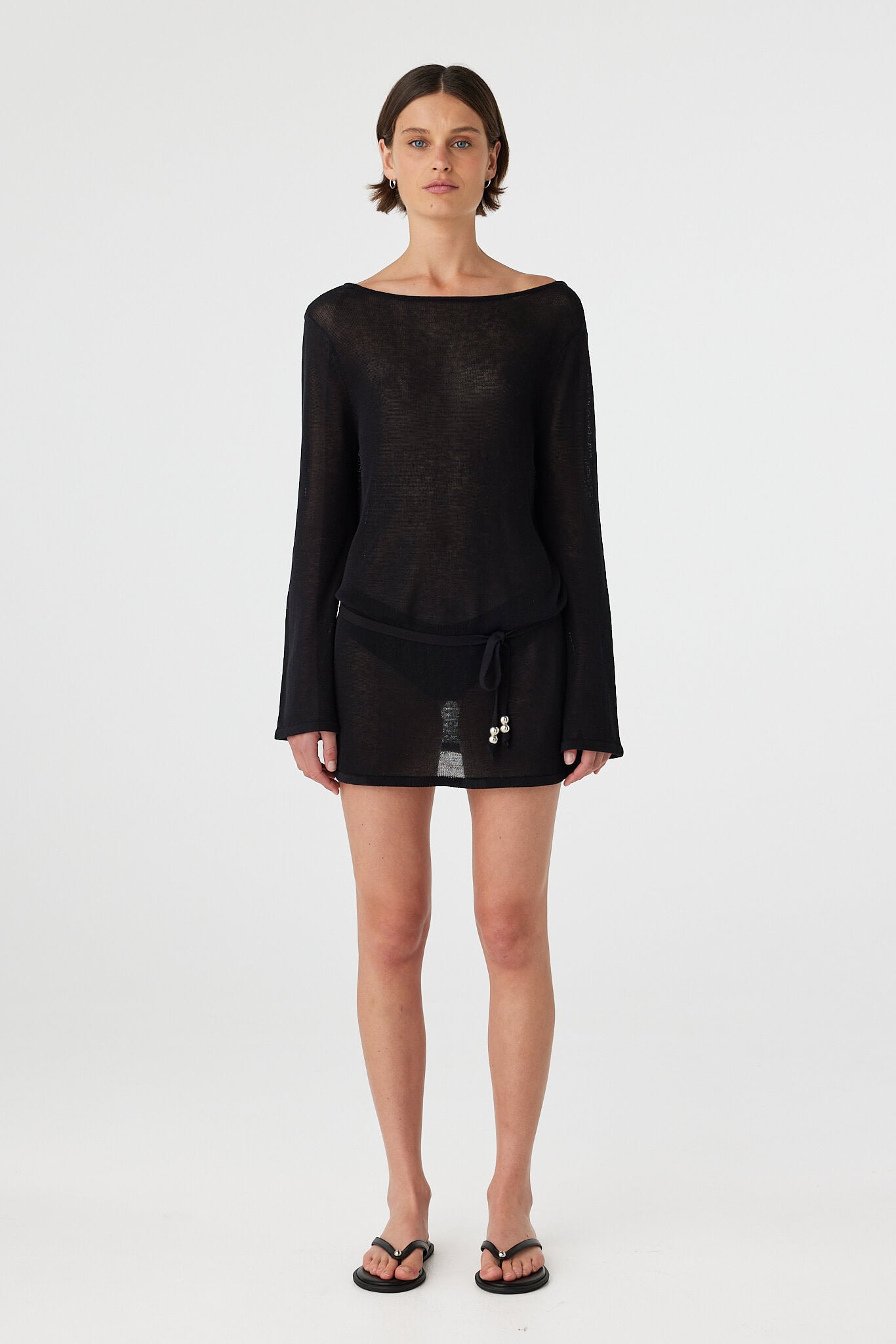 Model wearing a sheer cotton long sleeve mini dress in black with a relaxed silhouette and mini length, styled as an easy swim layer for warm weather.