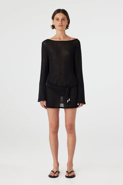 Model wearing a sheer cotton long sleeve mini dress in black with a relaxed silhouette and mini length, styled as an easy swim layer for warm weather.