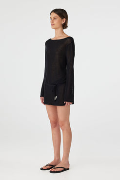 Side view of a loose-fit sheer cotton mini dress in black, showing fluid drape, lightweight knit texture and breathable feel for coastal wear.