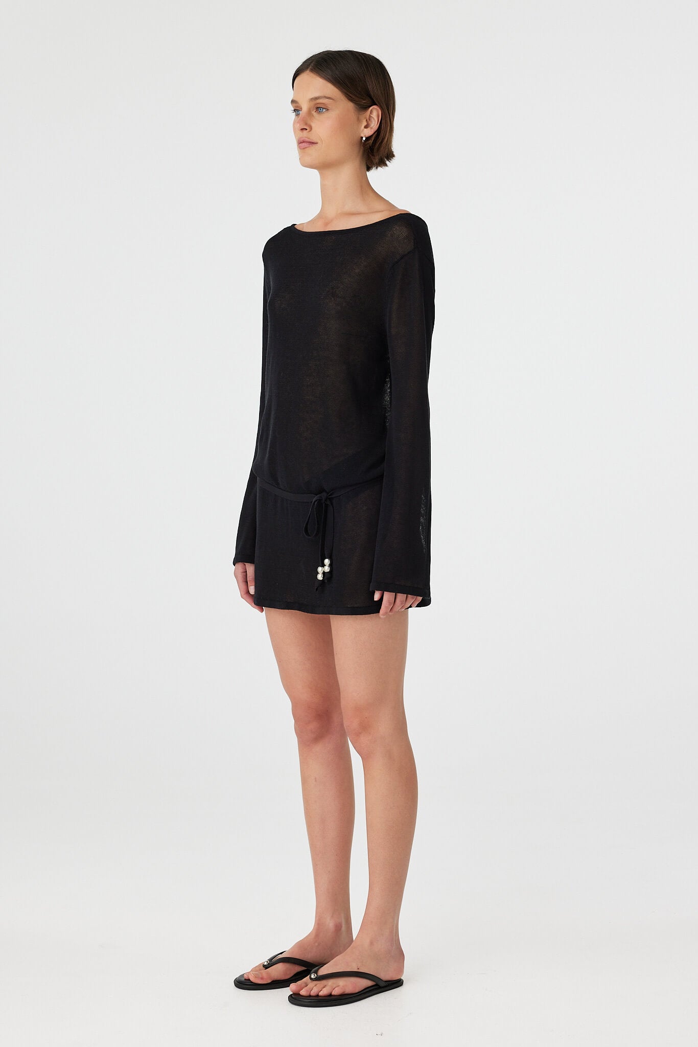 Side view of a loose-fit sheer cotton mini dress in black, showing fluid drape, lightweight knit texture and breathable feel for coastal wear.