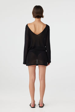 Back view of a reversible sheer cotton mini dress in black, worn with a deeper neckline to show flexible styling and light coverage.
