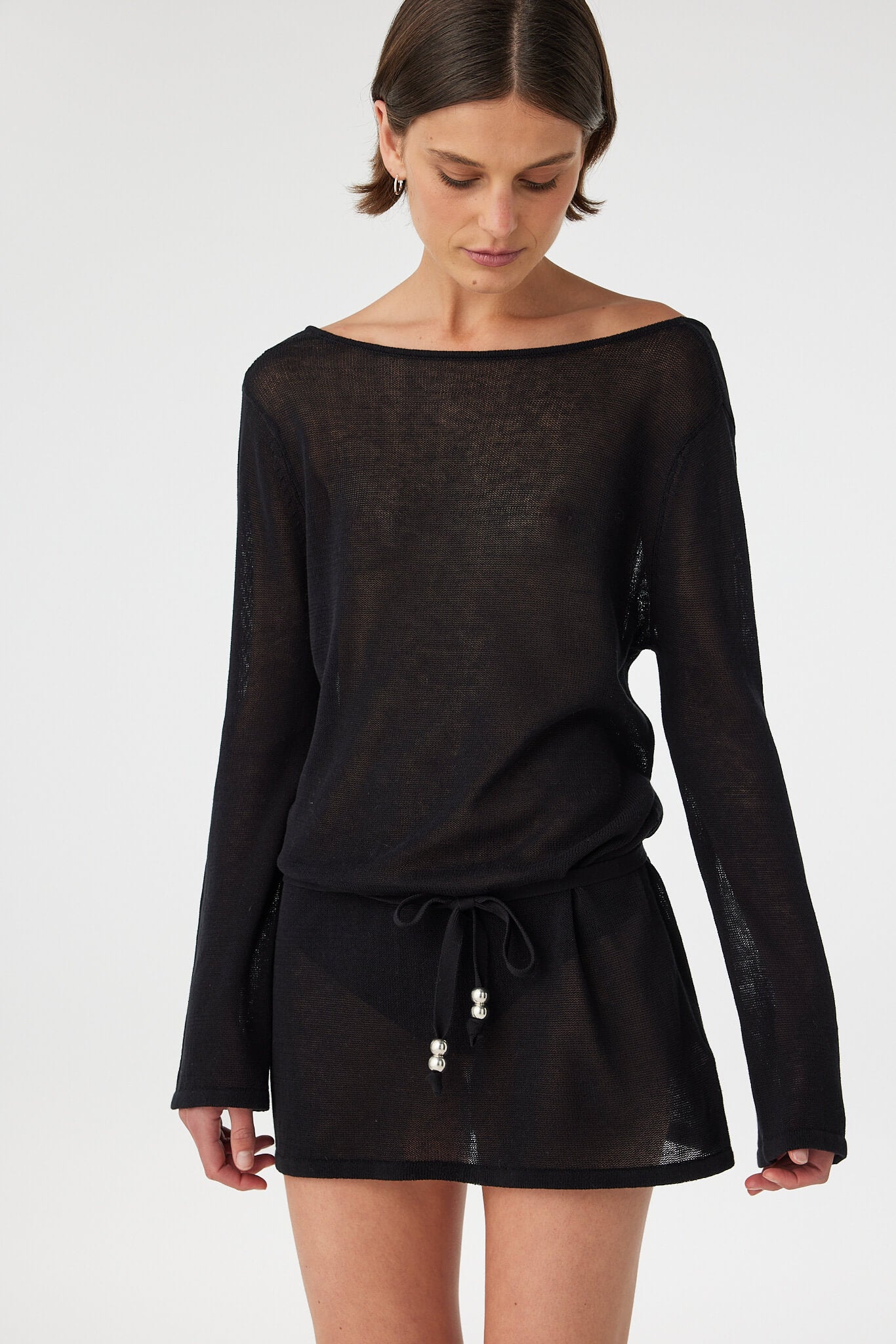 Sheer black cotton long sleeve mini dress with a loose fit and boat neckline, lightweight knit designed for layering over swimwear in warm coastal climates.