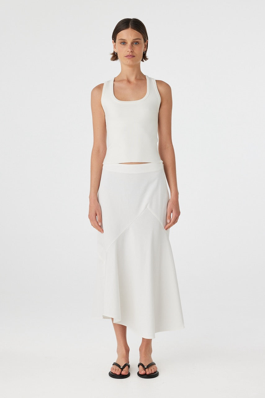 Model wearing cream cotton–Tencel twill skirt with fitted waist, asymmetrical bias-cut hem, and soft A-line shape.