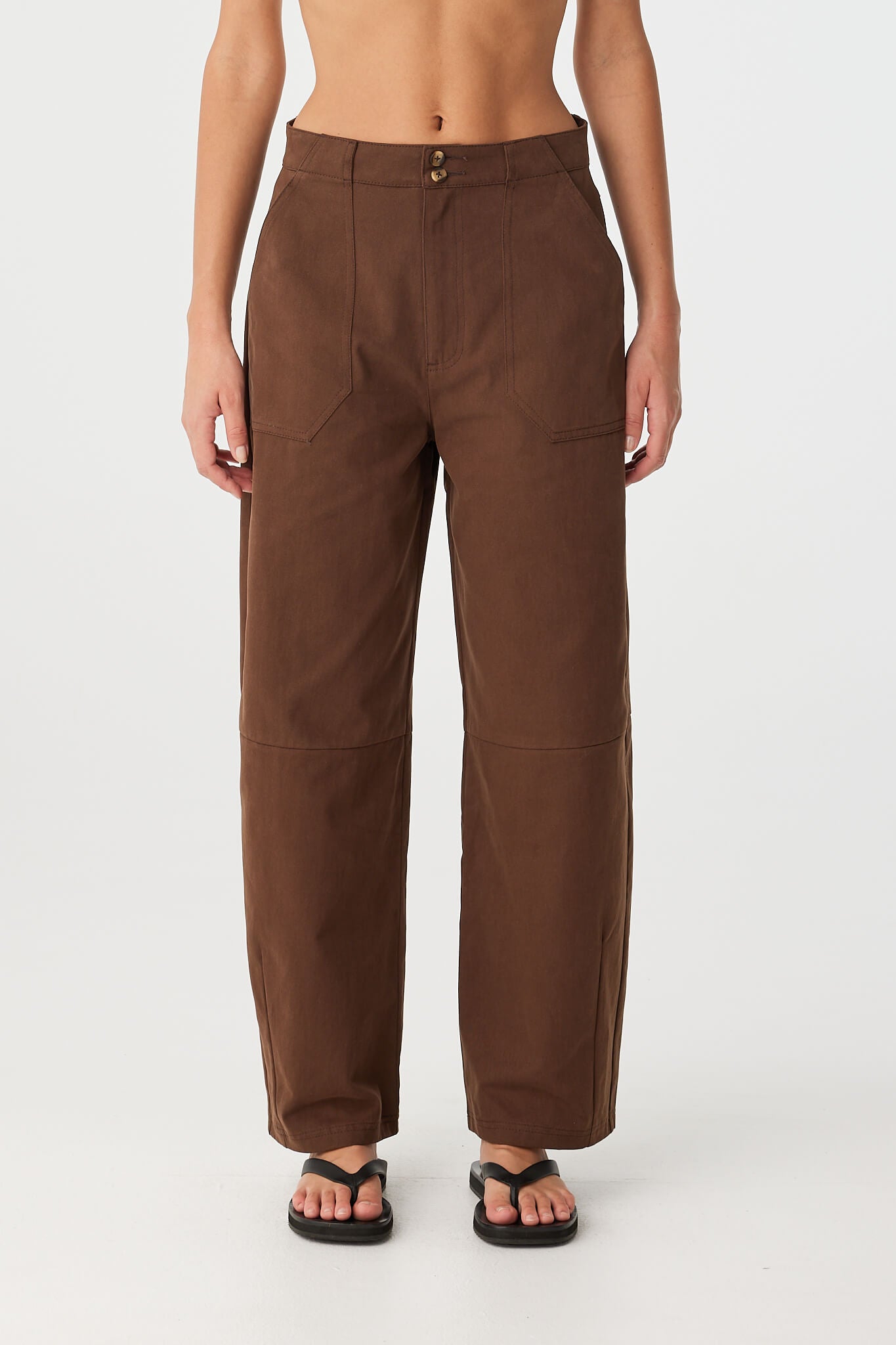 Close-up of chocolate barrel-leg cotton pants with darted legs and front patch pockets.