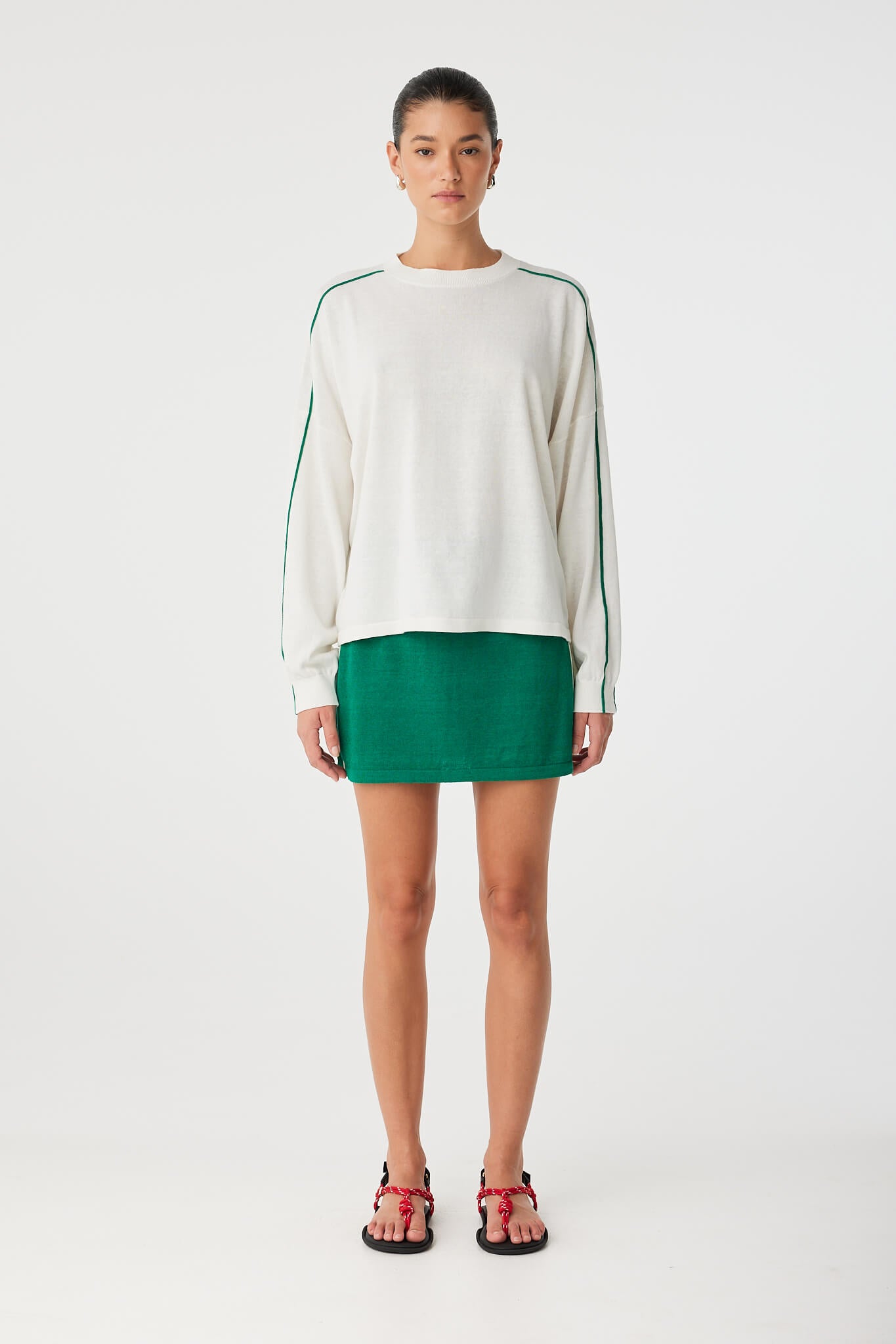 Full-body shot of cream long sleeve tee with contrast stripes, styled with green mini skirt.