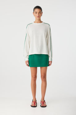 Full-body shot of cream long sleeve tee with contrast stripes, styled with green mini skirt.