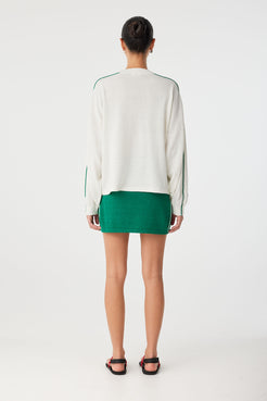 Back view of knit long sleeve tee in cream, styled with matching green mini skirt.