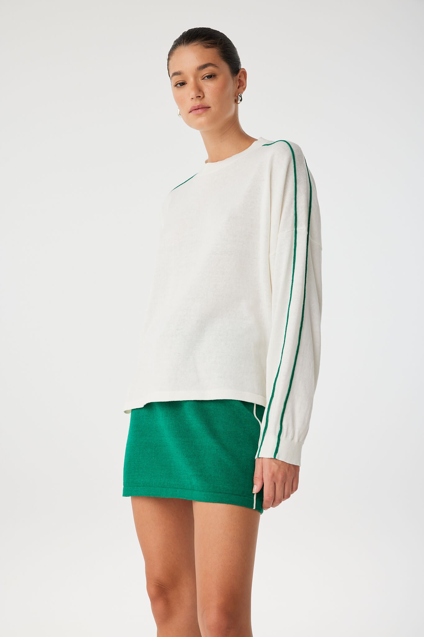 Side angle of slouchy knit tee styled with green mini skirt, showing soft drape and stripe.