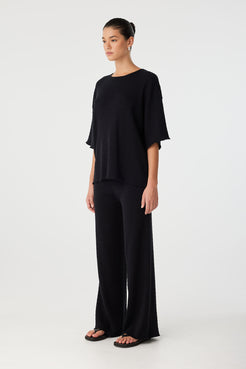 Three-quarter view of black knit pants styled for relaxed modern comfort.