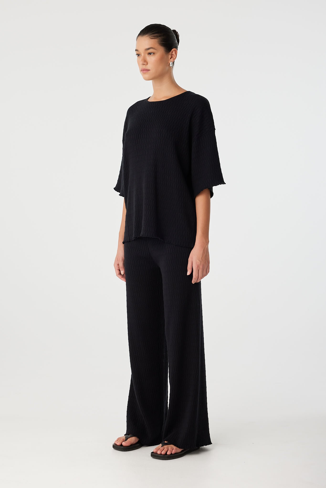 Three-quarter view of black knit pants styled for relaxed modern comfort.